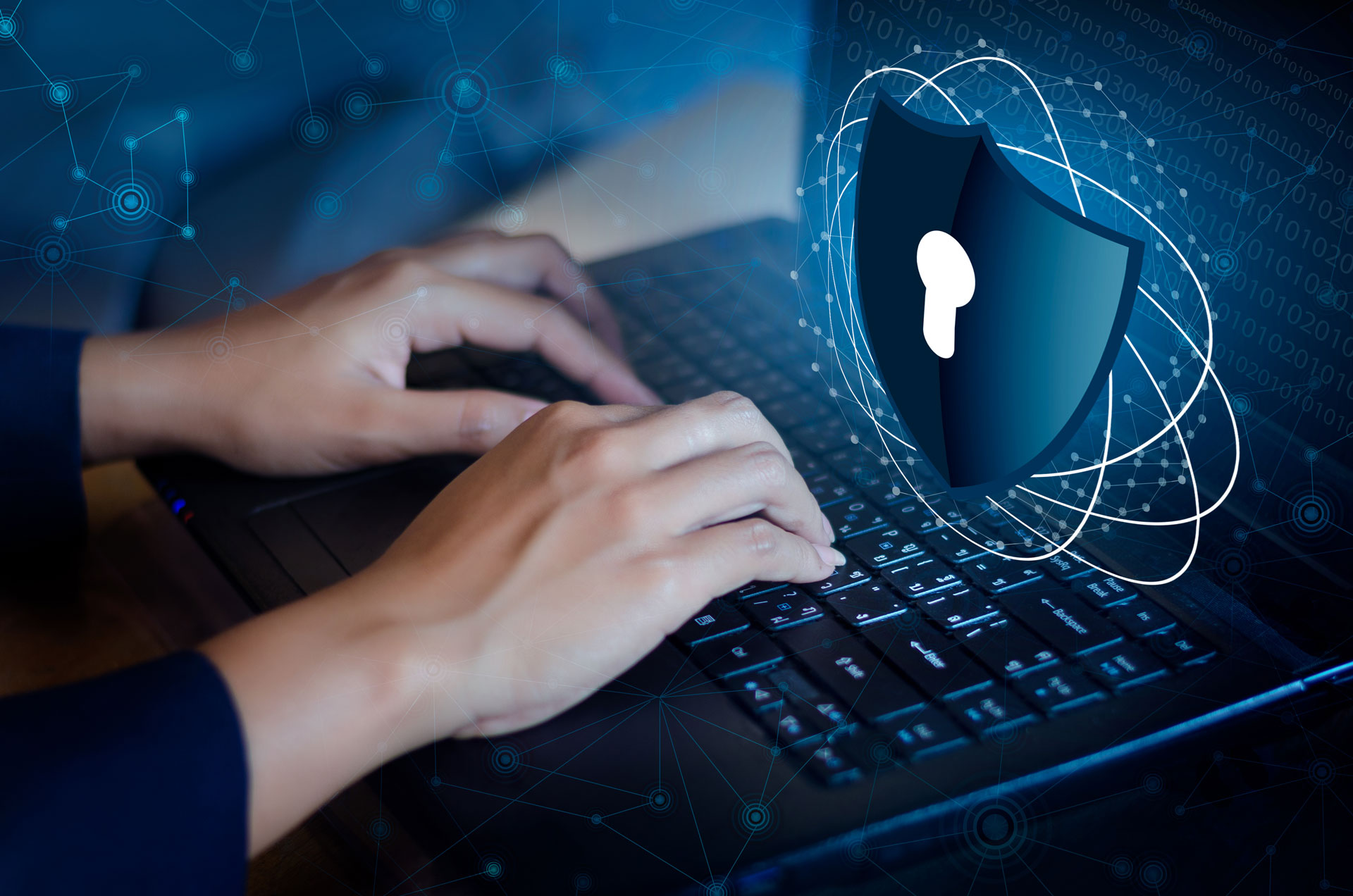 The Atomic Wallet Hack and the Risks it Reveals Picture of someone typing on a laptop with a graphic of a shield with a keyhole in the middle floating above the laptop. The picture has a overlay of transparent like circles and lines